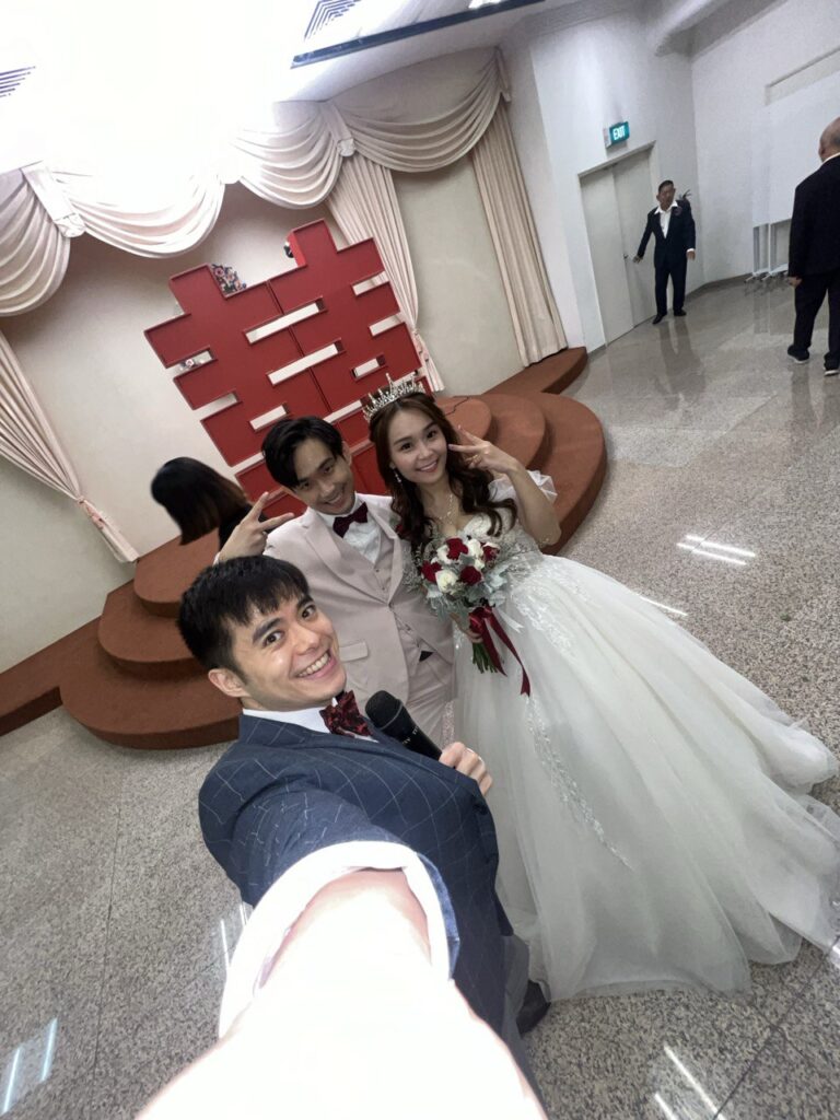 0.5x selfie of the wedding emcee with a happy couple, at a wedding banquet held in a Chinese temple in Singapore.